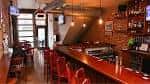 Interior del bar con barra de madera y sillas rojas