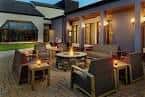 Área exterior del patio con mobiliario de jardín, mesas con velas y acceso a salas interiores
