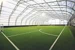 Interior de una cancha deportiva cubierta con césped artificial y estructura metálica