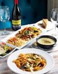 Mesa servida con platos de pasta, ensalada, vino tinto y pan en ambiente elegante