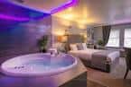 Interior de una suite con jacuzzi iluminado en tonos púrpuras y cama doble