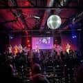 Interior del venue con banda en escena, luces rojas y disco ball