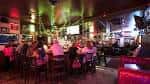 Interior del bar con ambiente nocturno, luces de colores y clientes sentados en mesas