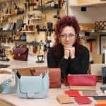 Mujer sentada en el taller rodeada de productos de cuero y materiales