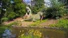 Escultura de dinosaurio junto a un estanque en el parque