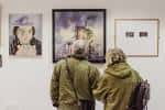 Dos visitantes observando una exposición de arte colgado en las paredes