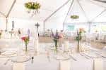 Interior de una carpa blanca decorada para una boda con mesas y centros de flores