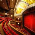 Interior del teatro mostrando las butacas rojas, el escenario con cortina roja y detalles ornamentales dorados en el techo