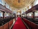 Interior de la nave principal con bancos de madera, alfombra roja y techo decorado con frescos dorados