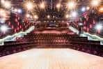 Vista general del interior del teatro con butacas rojas y escenario iluminado
