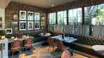 Área de comedor interior con mesas, sillas tapizadas y ventanas grandes