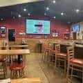 Interior del bar con mesas, sillas altas y pantalla de televisión en la pared