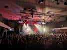 Interior del local con escenario iluminado y público asistiendo a un evento