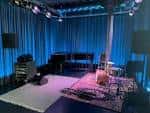 Interior del club con escenario iluminado en azul, piano y equipo musical listo para el espectáculo