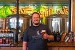 Persona sosteniendo una copa de cerveza frente a tanques de fermentación