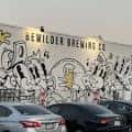 Fachada iluminada de Bewilder Brewing Co. con mural artístico y coches estacionados