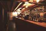 Interior del Stocks Bar con barra larga, estanterías de botellas y techo de vigas de madera