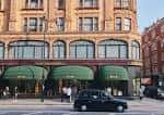 Vista exterior diurna de la entrada principal de Harrods con toldos verdes y tráfico urbano