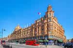 Panorámica del edificio Harrods en un día soleado con autobús rojo y bandera francesa