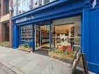 Fachada azul de Bird & Blend Tea Co. con entrada abierta y escaparate iluminado