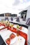 Mesa decorada con mantel blanco y detalles naranjas en la terraza del lugar