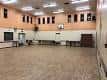 Sala polivalente vacía con suelo de madera y canasta de baloncesto en la pared