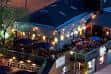 Vista exterior nocturna de Gracie's con terraza iluminada y mesas al aire libre