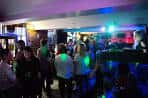Interior del bar con ambiente nocturno, luces de colores y personas disfrutando