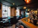 Interior del bar con barra de madera y mesas junto a ventana