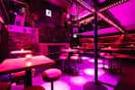 Interior del local con mesas y sillas bajo iluminación púrpura