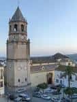 Vista exterior de la Iglesia de San Juan Bautista en Vélez-Málaga, mostrando su torre campanario y fachada principal al atardecer