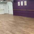 Interior de un estudio de danza con suelo de madera y barra en pared morada