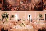 Salón de banquetes con mesas redondas, mantelería blanca y murales históricos en las paredes