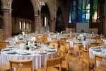 Salón interior de la iglesia decorado para evento con mesas redondas cubiertas de blanco y sillas de madera