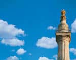 Detalle superior del Monumento mostrando la llama dorada contra el cielo azul