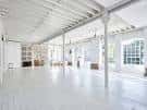 Espacio blanco vacío tipo loft con vigas industriales y suelo de madera