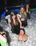 Interior del bar con personas en una piscina de bolas bajo luces de fiesta