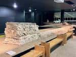 Restos arqueológicos del anfiteatro romano expuestos en el interior del centro de visitantes con bancos de madera