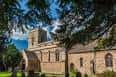 Fachada principal de la iglesia rodeada de árboles frondosos bajo un cielo azul