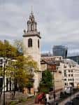 Vista exterior de la iglesia St James Garlickhythe con su torre característica y el skyline moderno de Londres al fondo