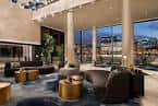 Área lounge interior del hotel con sofás modernos, mesas doradas y grandes ventanales con vista a la ciudad