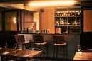 Interior del bar con estantería de botellas y mesas para clientes