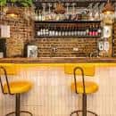 Barra interior con taburetes amarillos y estantería de bebidas