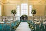 Sala decorada para una ceremonia con sillas blancas, pasillo central y arreglos florales