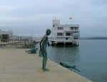 Escultura junto al muelle con embarcación blanca en el puerto