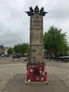 Detalle superior del obelisco con escultura de aves y base decorada con flores rojas