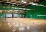 Pista deportiva interior del Redbridge Sports Centre con suelo de madera y redes de voleibol