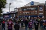 Entrada principal del estadio Selhurst Park con aficionados entrando al recinto