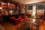 Interior del bar con barra de madera, estanterías llenas de botellas y sofás rojos