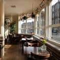 Interior del bar con mesas junto a ventanas grandes y decoración cálida